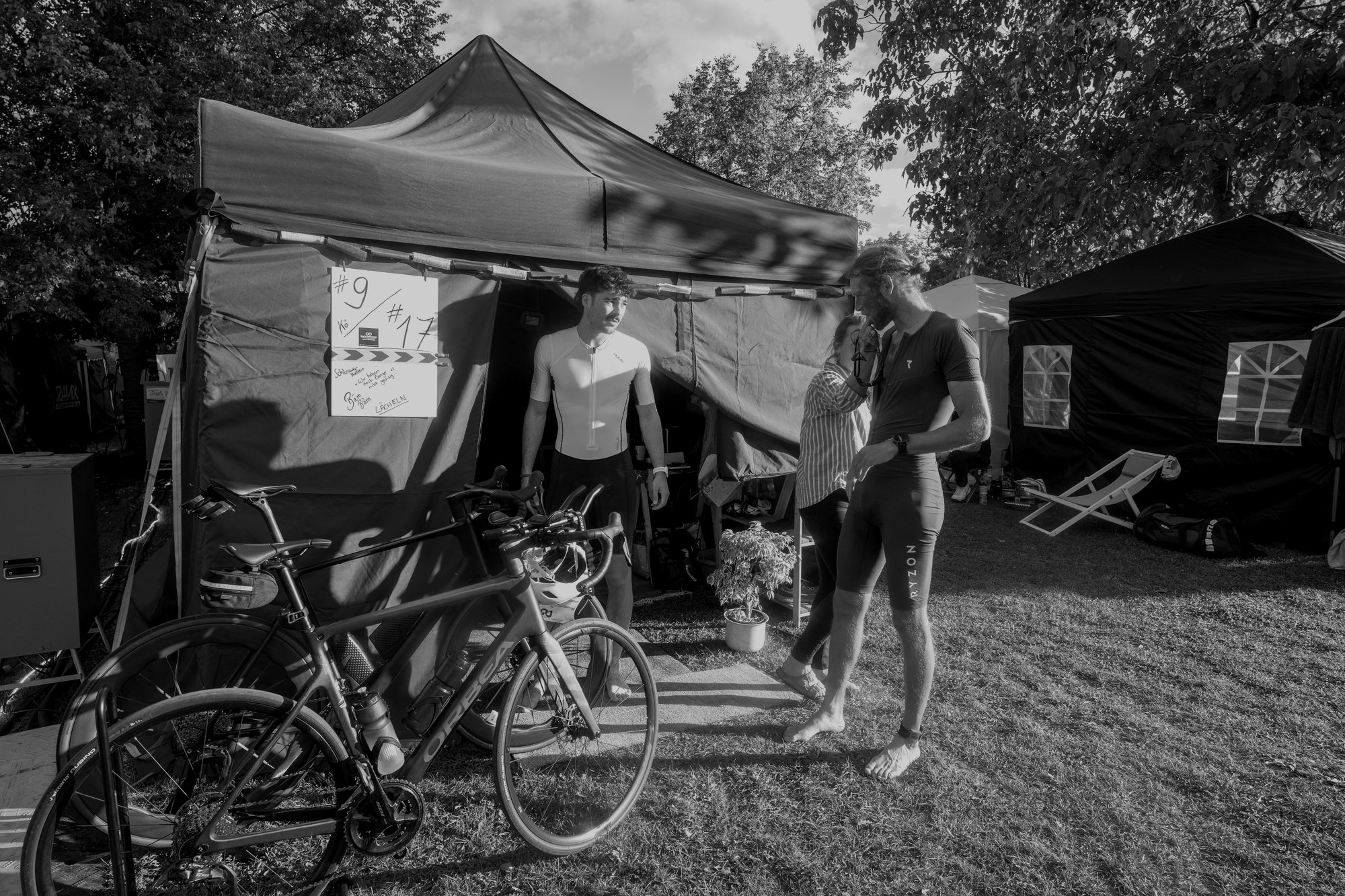 Athlet im Gespräch mit seiner Crew vor dem Camp-Zelt, Rennrad im Vordergrund